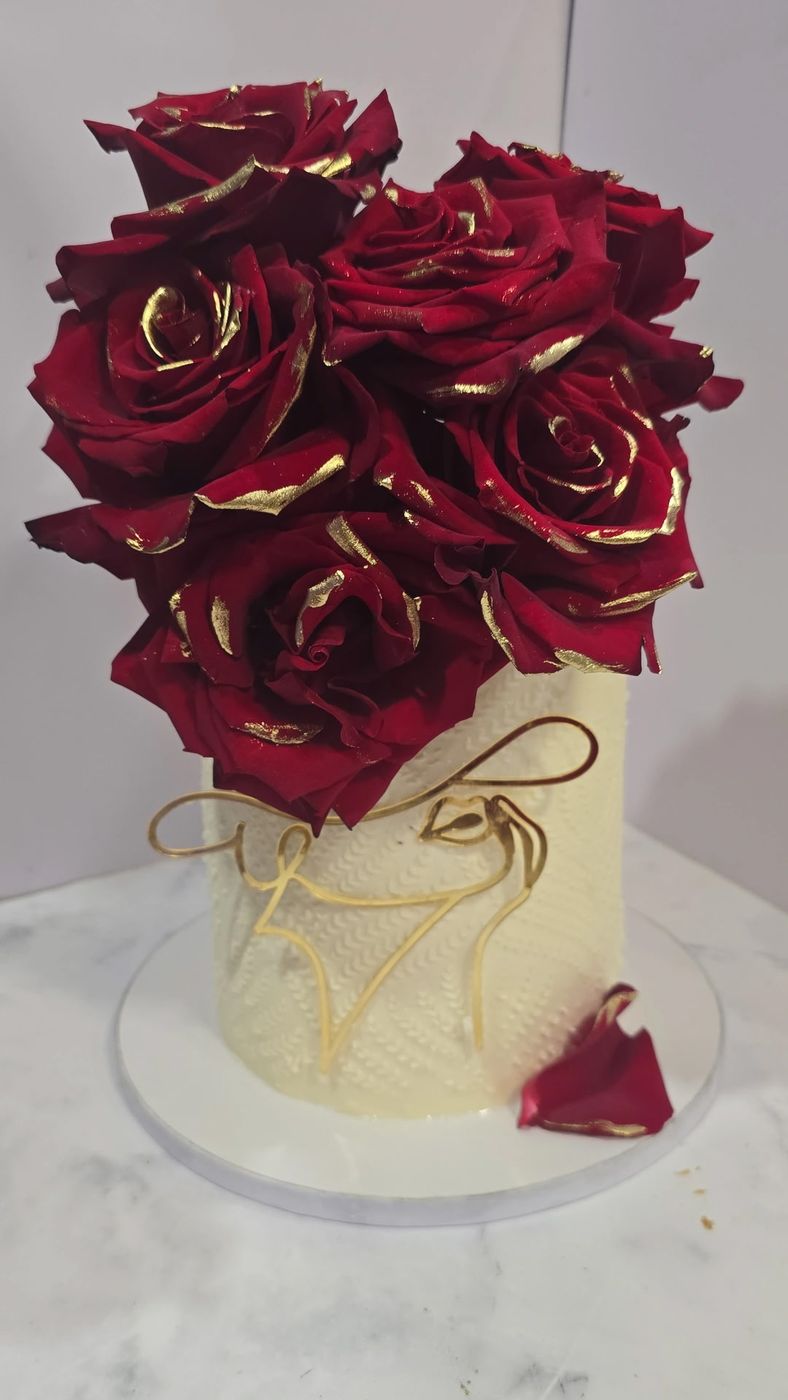 Cream cake topped with a bouquet of deep red roses brushed with gold
