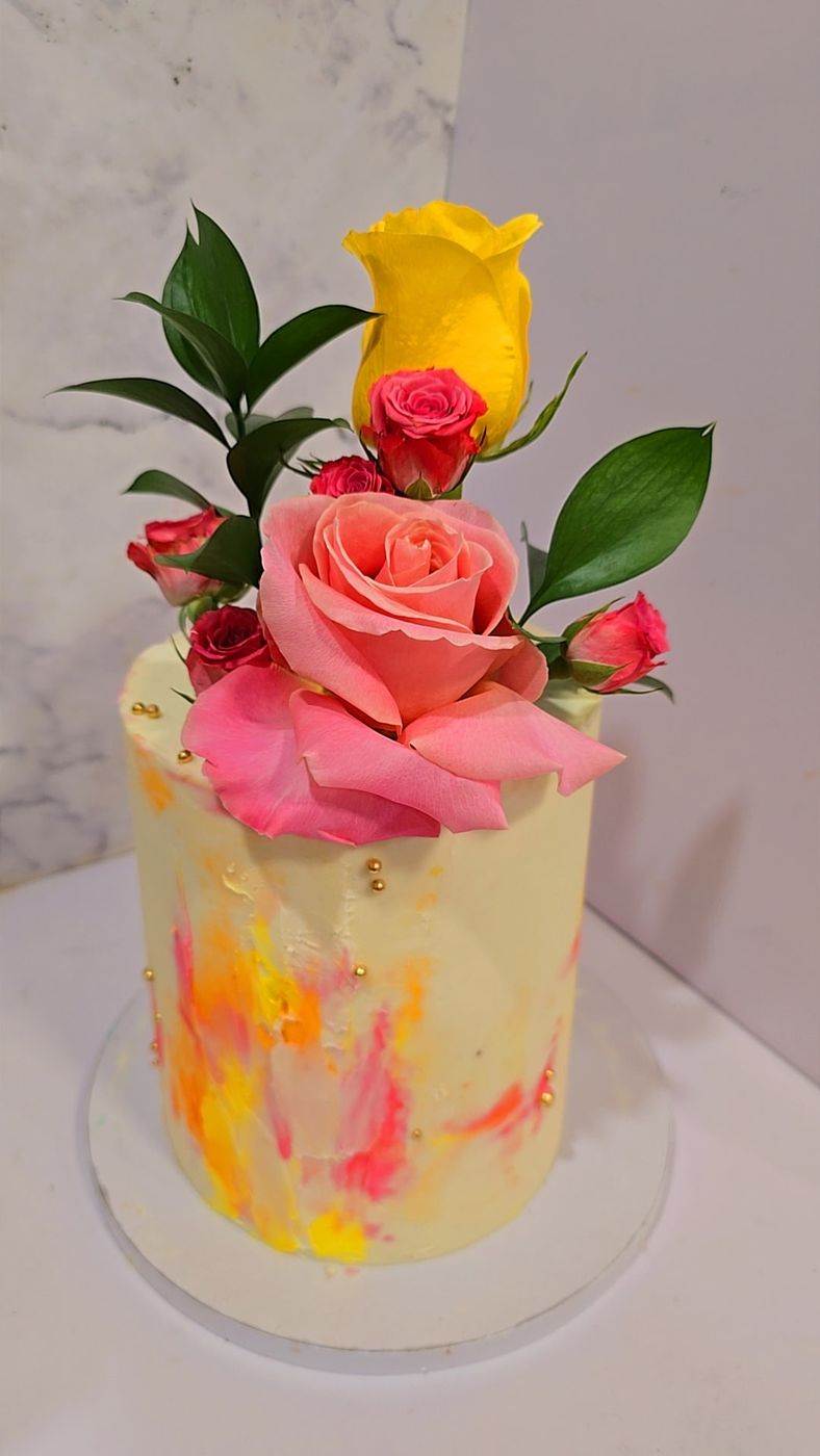 Watercolor yellow cake topped with a yellow rose, pink rose and greenery