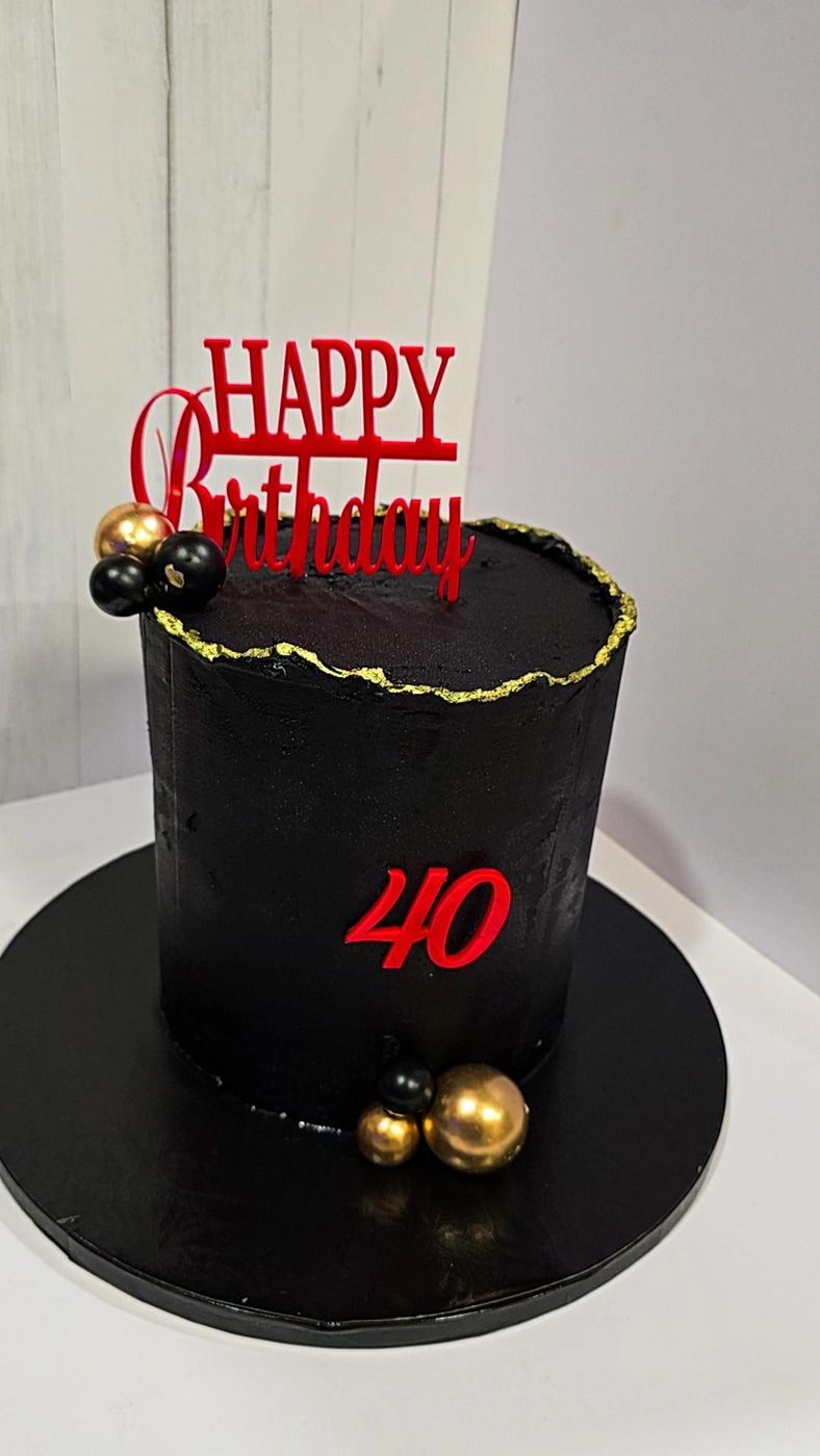 Black birthday cake with gold accents, a red 40 and a red Happy Birthday topper