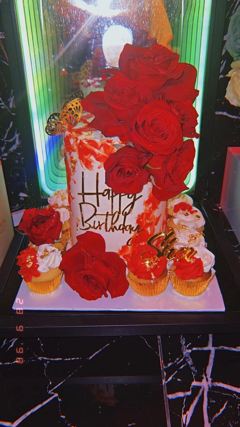 Tall white birthday cake with red roses beside matching cupcakes