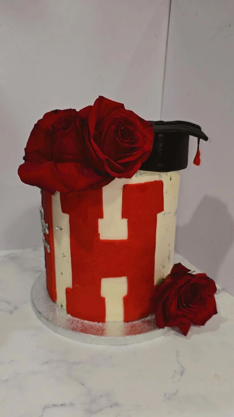 Red and white graduation cake with a letter H, a cap and red roses